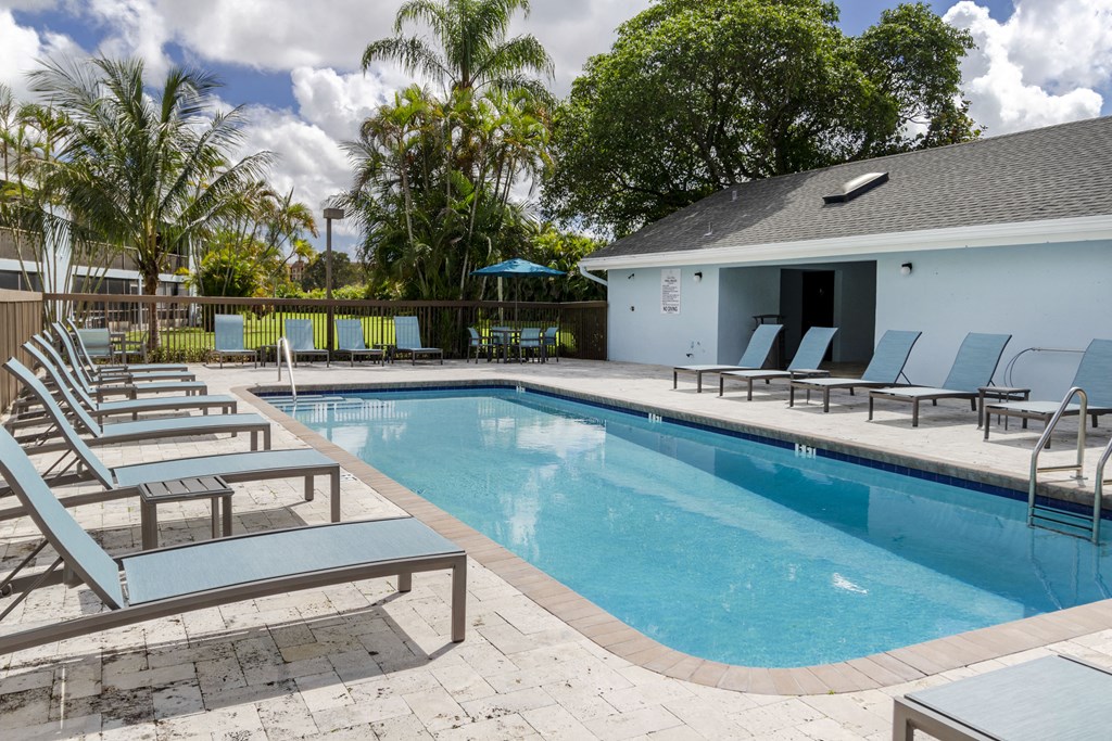 A pool with sun loungers and a building in the background.